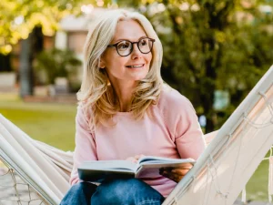 middle aged woman reading with glasses outside laying on a hammock