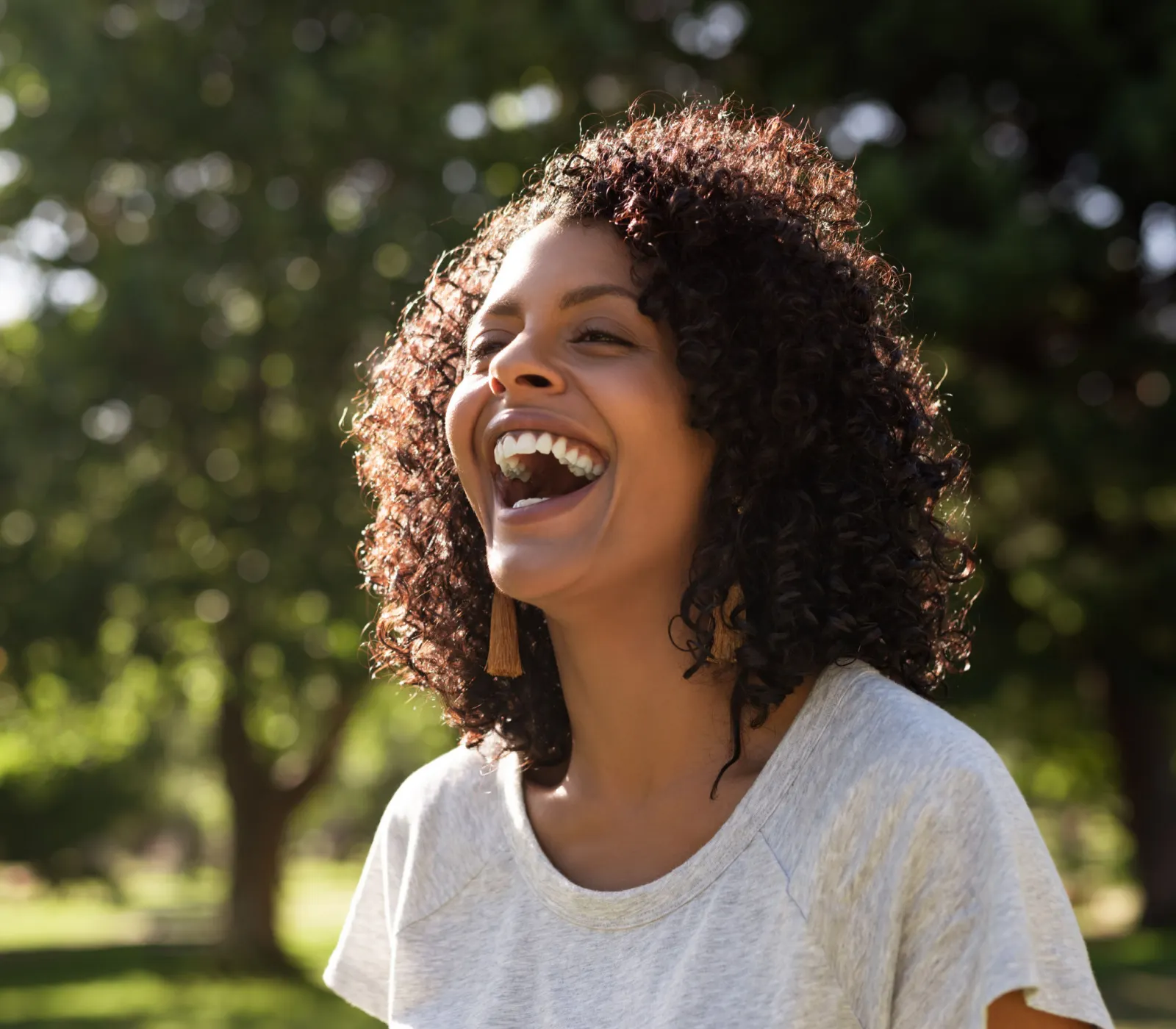 Young healthy woman with curly hair laughing while standing outside in a park on a sunny summer afternoon